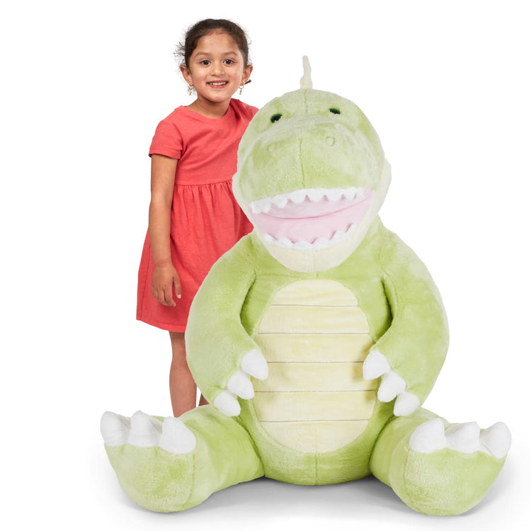 A child on white background with the Melissa & Doug Gentle Jumbos Dinosaur Giant Stuffed Plush Animal (Sits Nearly 3 Feet Tall)