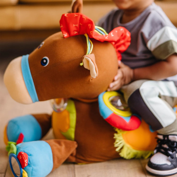 A kid playing with the Melissa & Doug Giddy-Up and Play Baby Activity Toy - Multi-Sensory Horse