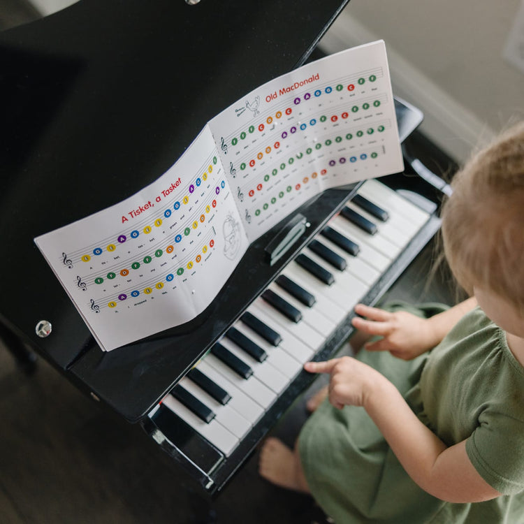 A kid playing with the Melissa & Doug Learn-To-Play Classic Grand Piano With 30 Keys, Color-Coded Songbook, and Non-Tip Bench