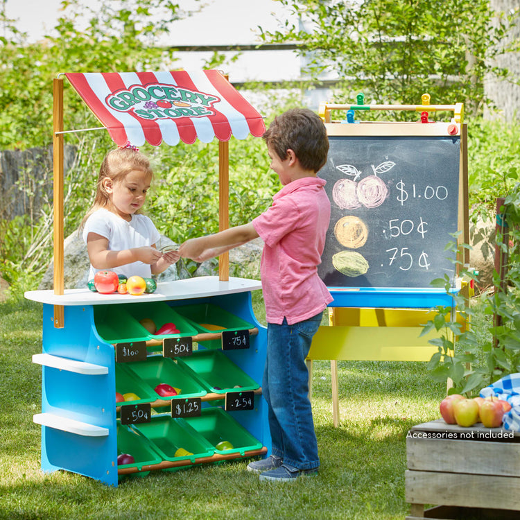 A kid playing with the Melissa & Doug Wooden Grocery Store and Lemonade Stand - Reversible Awning, 9 Bins, Chalkboards
