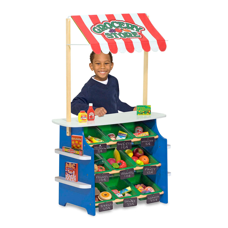 A child on white background with the Melissa & Doug Wooden Grocery Store and Lemonade Stand - Reversible Awning, 9 Bins, Chalkboards