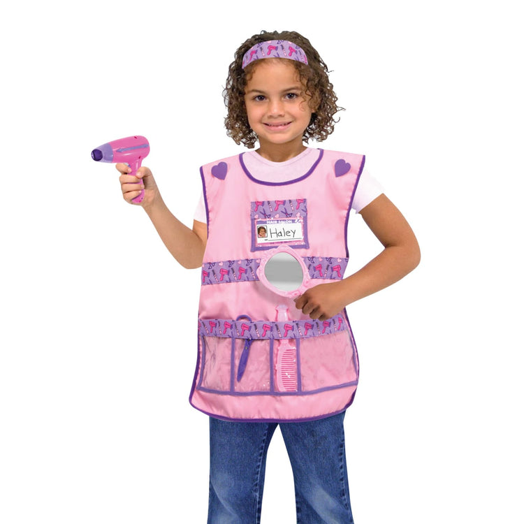 A child on white background with the Melissa & Doug Hair Stylist Role Play Costume Dress-Up Set (7 pcs)