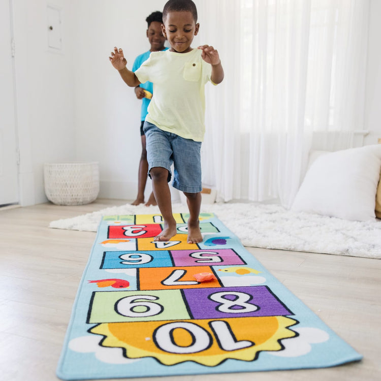 A kid playing with the Melissa & Doug Hop and Count Hopscotch Game Rug  (3 pcs, 78.5 x 26.5 inches)