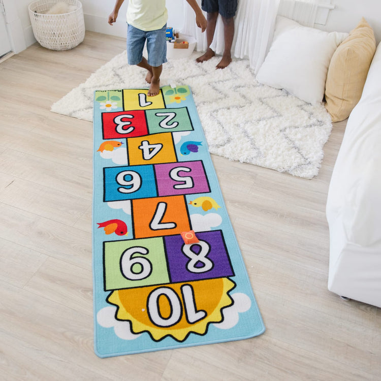 A kid playing with the Melissa & Doug Hop and Count Hopscotch Game Rug  (3 pcs, 78.5 x 26.5 inches)