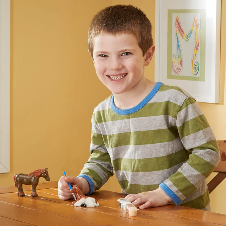 A kid playing with the Melissa & Doug Created by Me! Horse Figurines Craft Kit (2 Resin Horses, 6 Paints, Paintbrush)