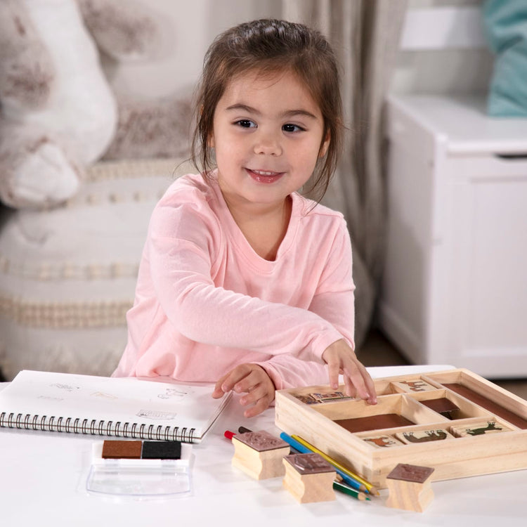 A kid playing with the Melissa & Doug Wooden Stamp Activity Set: Horses - 10 Stamps, 5 Colored Pencils, 2-Color Stamp Pad