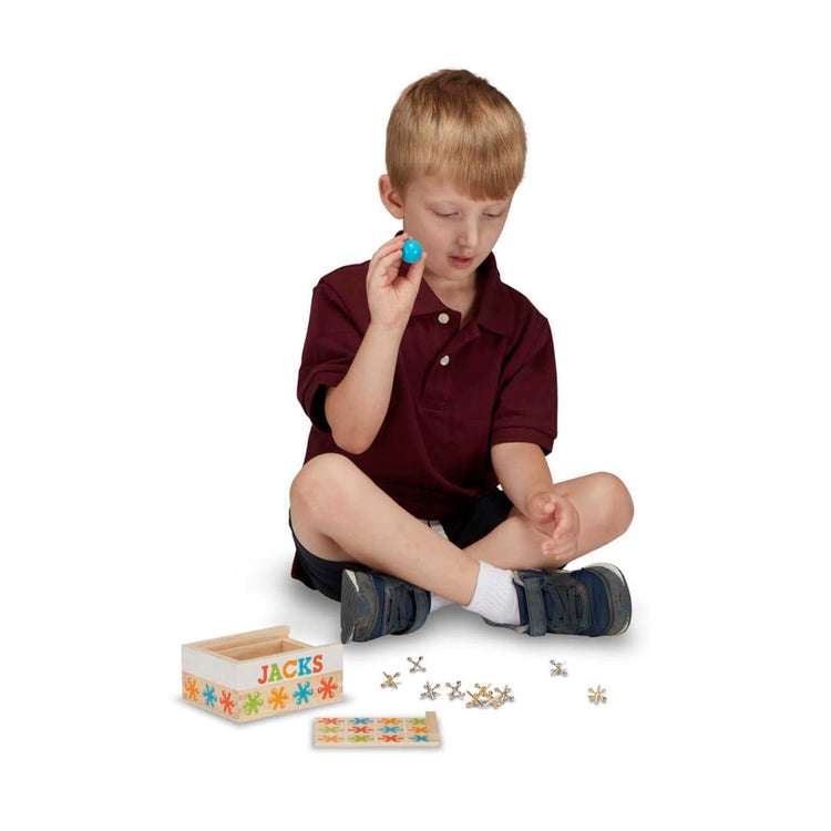 A child on white background with the Melissa & Doug Jacks Game with 10 Playing Pieces and 2 Balls in Wooden Storage Box