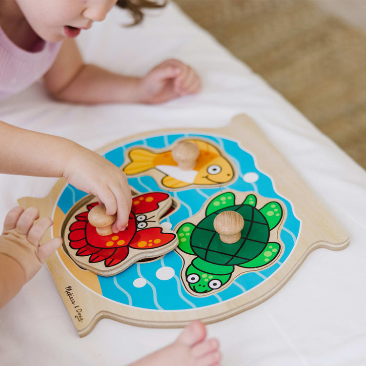 A kid playing with the Melissa & Doug Animals Jumbo Peg Wooden Puzzles 2-Pack - Fish and Pets