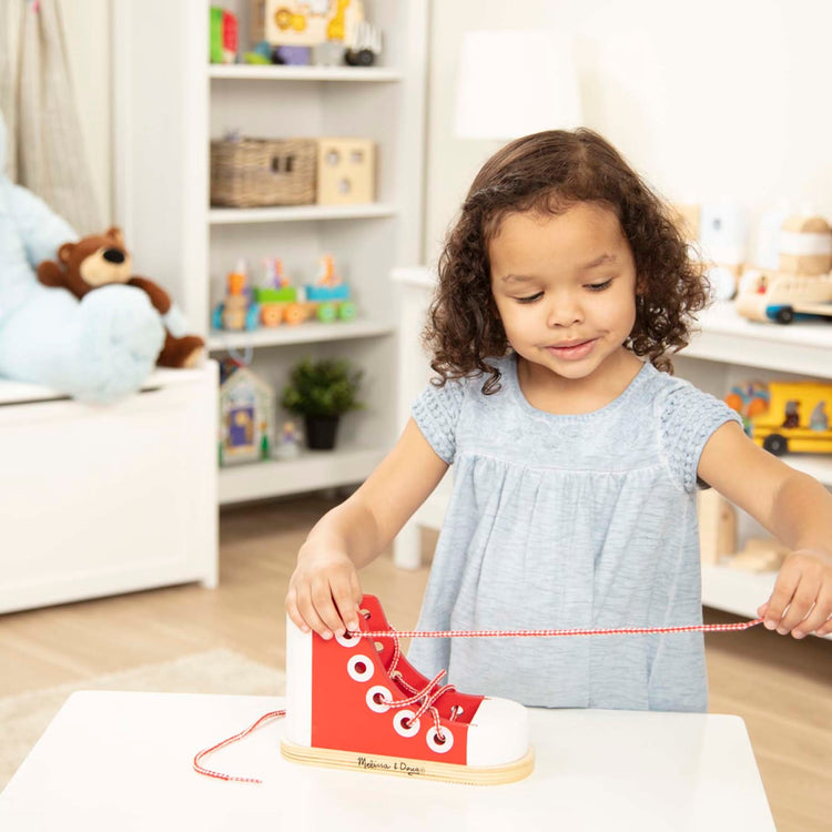 A kid playing with the Melissa & Doug Wooden Lacing Shoe- Learn to Tie a Shoe Educational Toy