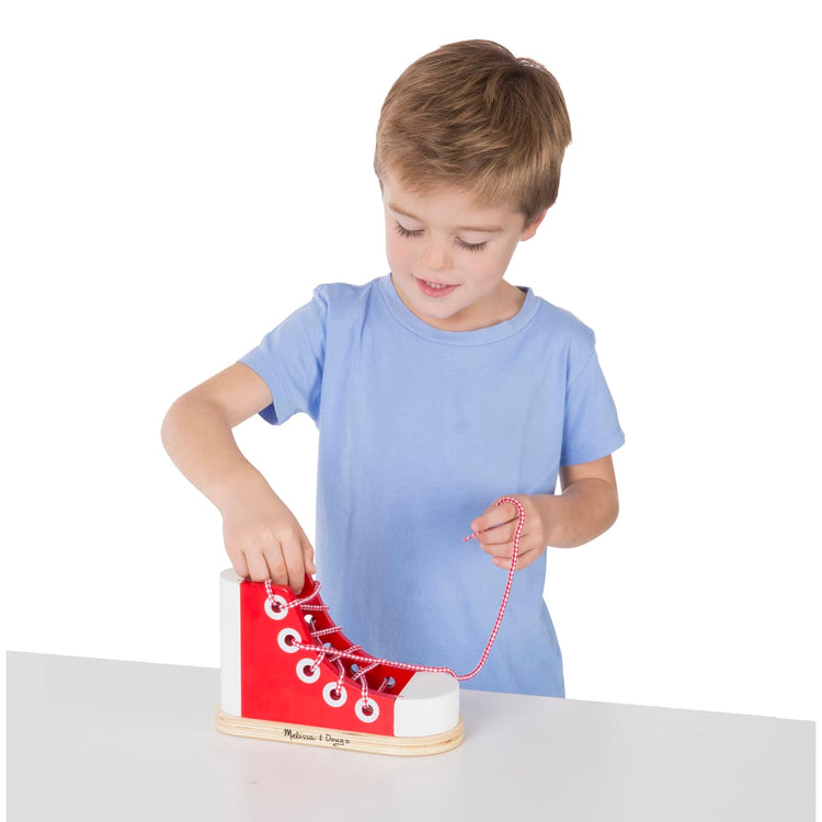 A child on white background with the Melissa & Doug Wooden Lacing Shoe- Learn to Tie a Shoe Educational Toy