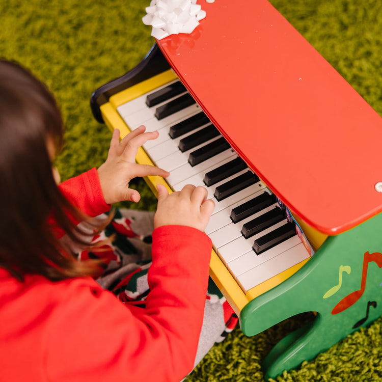 A kid playing with the Melissa & Doug Learn-To-Play Toy Piano With 25 Keys and Color-Coded Songbook