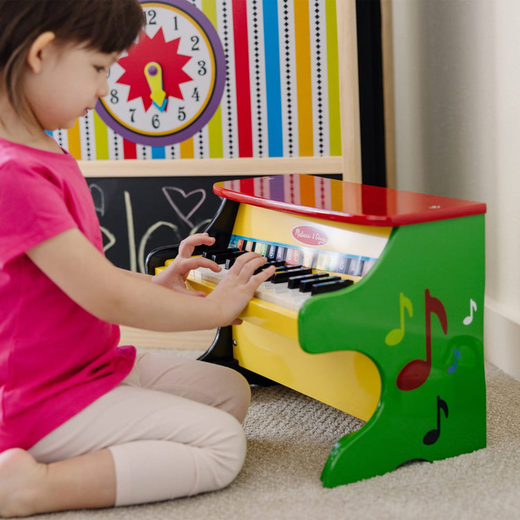 A kid playing with the Melissa & Doug Learn-To-Play Toy Piano With 25 Keys and Color-Coded Songbook