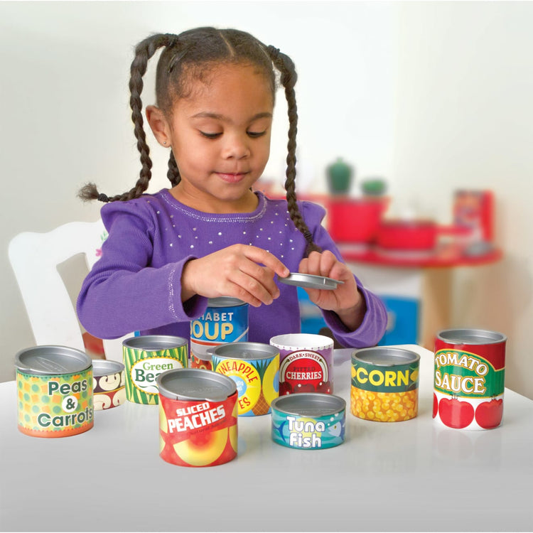 A kid playing with the Melissa & Doug Let's Play House! Grocery Cans Play Food Kitchen Accessory - 10 Stackable Cans With Removable Lids