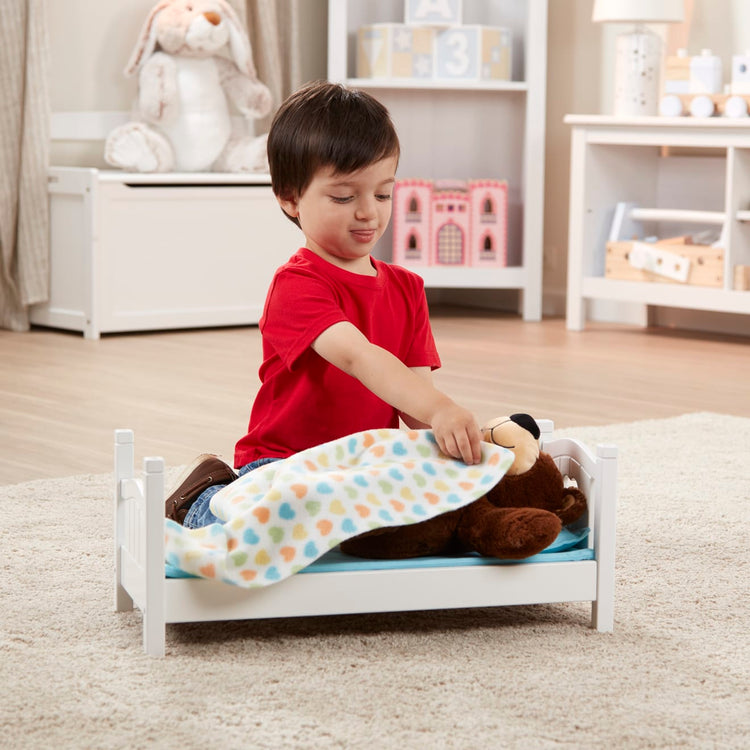 A kid playing with the Melissa & Doug Mine to Love Wooden Play Bed for Dolls, Stuffed Animals - White (8.7”H x 9.1”W x 20.7”L Assembled)