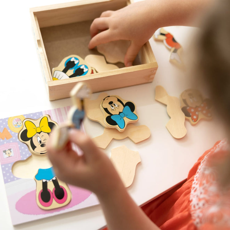 A kid playing with the Melissa & Doug Disney Minnie Mouse Mix and Match Dress-Up Wooden Play Set (18 pcs)