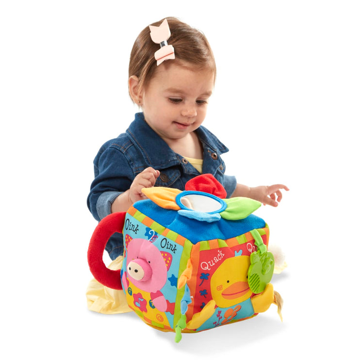 A child on white background with the Melissa & Doug K's Kids Musical Farmyard Cube Educational Baby Toy
