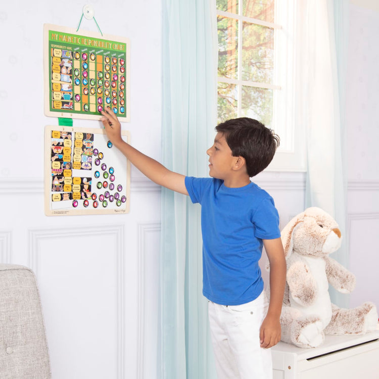 A kid playing with the Melissa & Doug Deluxe Wooden Magnetic Responsibility Chart With 90 Magnets