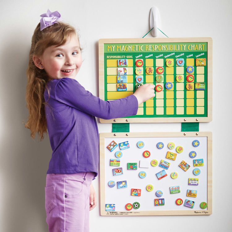 A kid playing with the Melissa & Doug Deluxe Wooden Magnetic Responsibility Chart With 90 Magnets