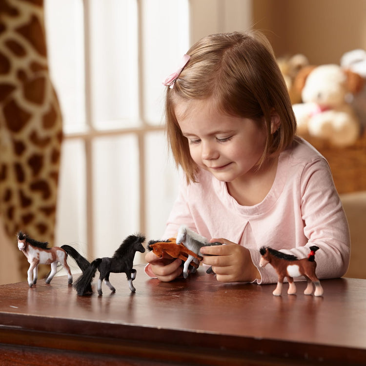 A kid playing with the Melissa & Doug Pasture Pals - 12 Collectible Horses With Wooden Barn-Shaped Crate