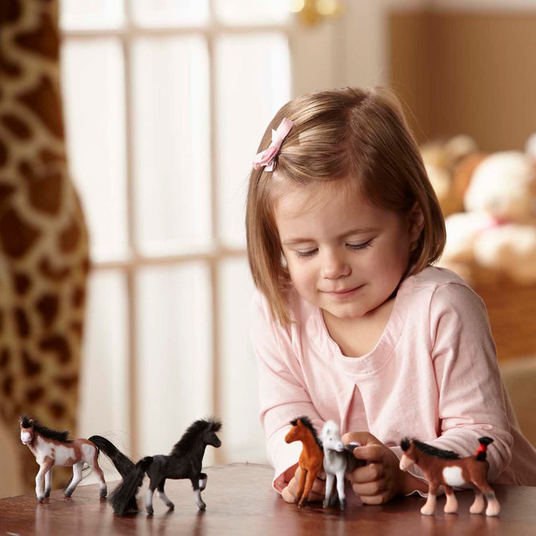 A kid playing with the Melissa & Doug Pasture Pals - 12 Collectible Horses With Wooden Barn-Shaped Crate