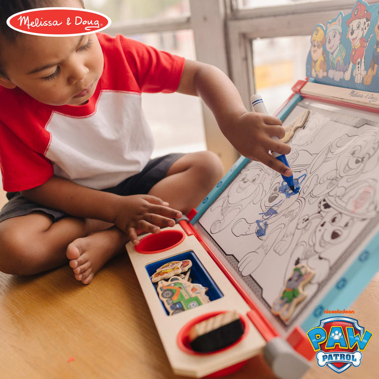 A kid playing with the Melissa & Doug PAW Patrol Wooden Double-Sided Tabletop Art Center Easel (33 Pieces)