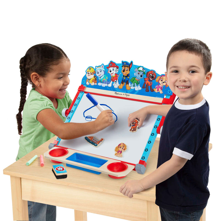 A child on white background with the Melissa & Doug PAW Patrol Wooden Double-Sided Tabletop Art Center Easel (33 Pieces)