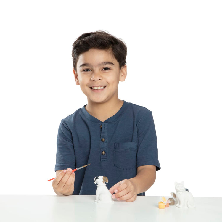 A child on white background with the Melissa & Doug Created by Me! Pet Figurines Craft Kit (Resin Dog and Cat, 6 Paints, Paintbrush)
