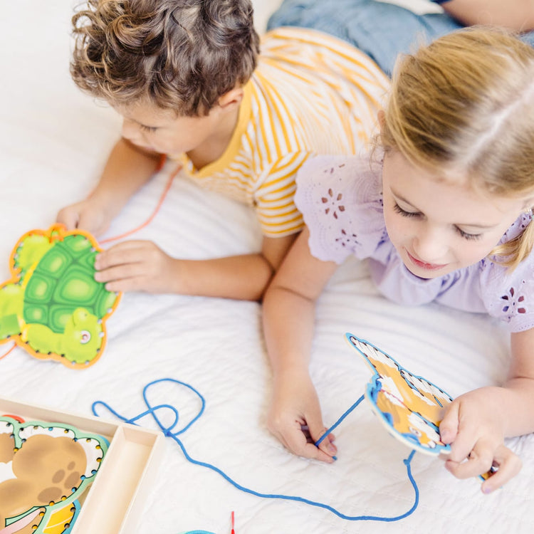 A kid playing with the Melissa & Doug Lace and Trace Activity Set: Pets - 5 Wooden Panels and 5 Matching Laces