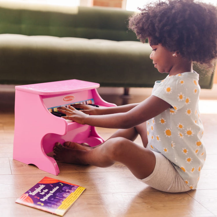 A kid playing with the Melissa & Doug Learn-to-Play Pink Piano With 25 Keys and Color-Coded Songbook