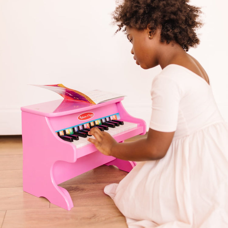 A kid playing with the Melissa & Doug Learn-to-Play Pink Piano With 25 Keys and Color-Coded Songbook