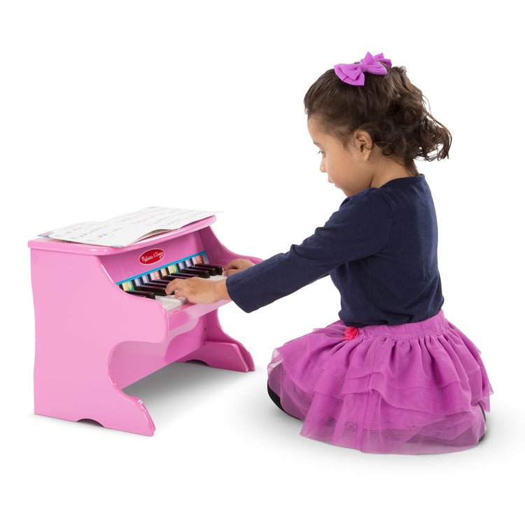 A child on white background with the Melissa & Doug Learn-to-Play Pink Piano With 25 Keys and Color-Coded Songbook