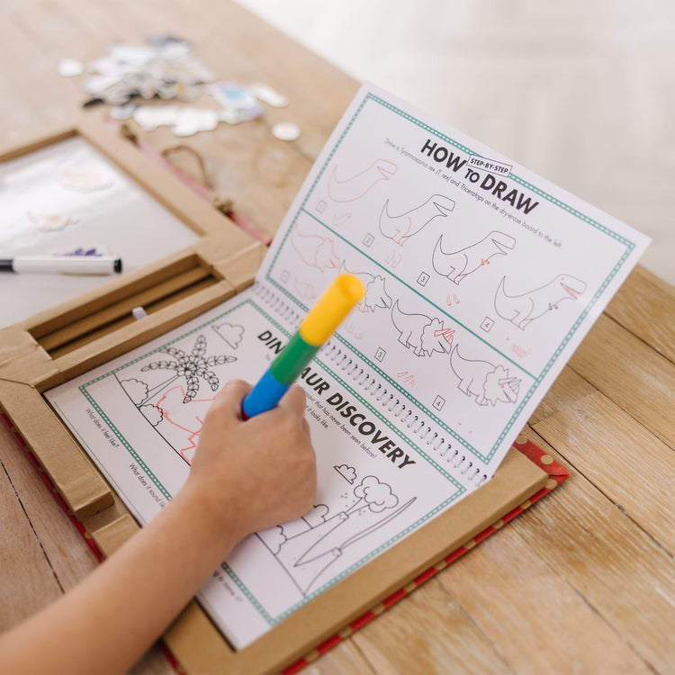 A kid playing with the Melissa & Doug Natural Play: Play, Draw, Create Reusable Drawing & Magnet Kit – Dinosaurs (41 Magnets, 5 Dry-Erase Markers)