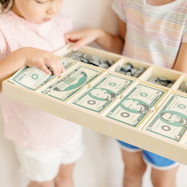 A kid playing with the Melissa & Doug Play Money Set - Educational Toy With Paper Bills and Plastic Coins (50 of Each Denomination) and Wooden Cash Drawer for Storage