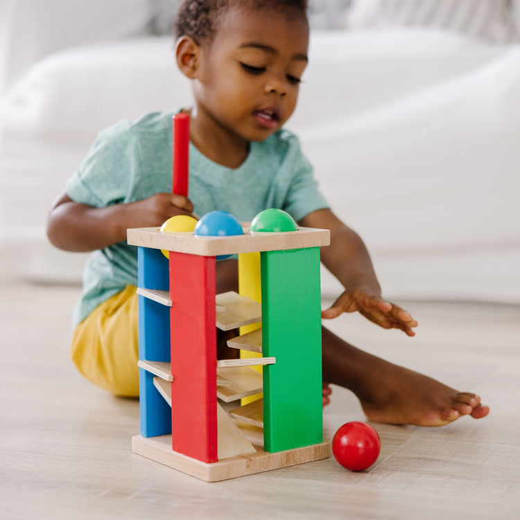 A kid playing with the Melissa & Doug Deluxe Pound and Roll Wooden Tower Toy With Hammer