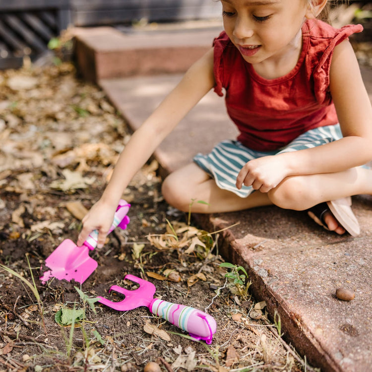 A kid playing with the Melissa & Doug Sunny Patch Pretty Petals Cultivator and Trowel Set, 2-Piece Children’s Metal Gardening Tools