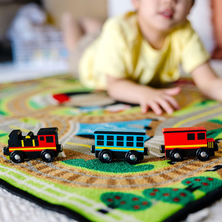 A kid playing with the Melissa & Doug Round the Rails Train Rug With 3 Linking Wooden Train Cars  (39 x 36 inches)