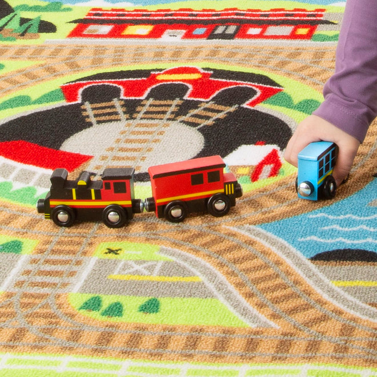 A child on white background with the Melissa & Doug Round the Rails Train Rug With 3 Linking Wooden Train Cars  (39 x 36 inches)