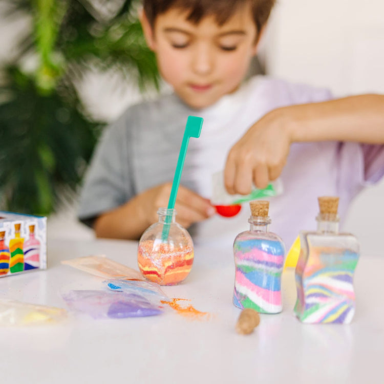 A kid playing with the Melissa & Doug Created by Me! Sand Art Bottles Craft Kit: 3 Bottles, 6 Bags of Colored Sand, Design Tool