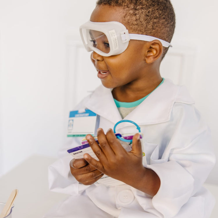 A kid playing with the Melissa & Doug Scientist Role Play Costume Set (X pcs) - Lab Coat, Goggles, 6 Experiments