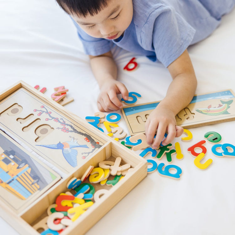 A kid playing with the Melissa & Doug See & Spell Wooden Educational Toy With 8 Double-Sided Spelling Boards and 64 Letters