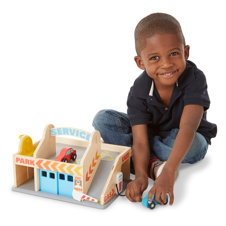 A child on white background with the Melissa & Doug Service Station Parking Garage With 2 Wooden Cars and Drive-Thru Car Wash