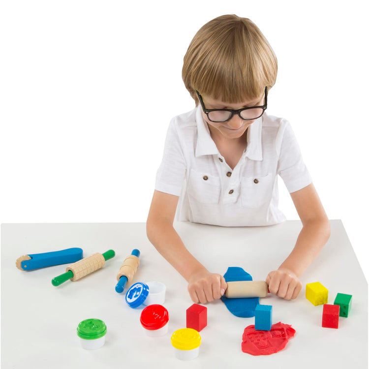 A child on white background with the Melissa & Doug Shape, Model, and Mold Clay Activity Set - 4 Tubs of Modeling Dough and Tools