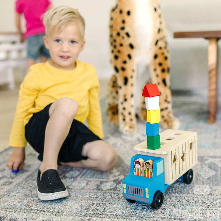 A kid playing with the Melissa & Doug Shape-Sorting Wooden Dump Truck Toy With 9 Colorful Shapes and 2 Play Figures