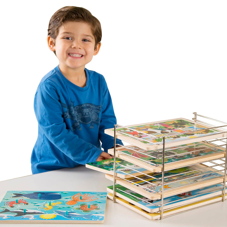 A child on white background with the Melissa & Doug Puzzle Storage Rack - Wire Rack Holds 12 Puzzles