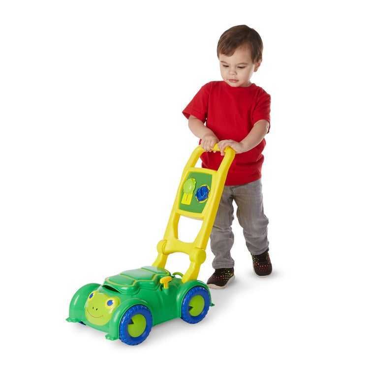 A child on white background with the Melissa & Doug Sunny Patch Snappy Turtle Lawn Mower - Pretend Play Toy for Kids