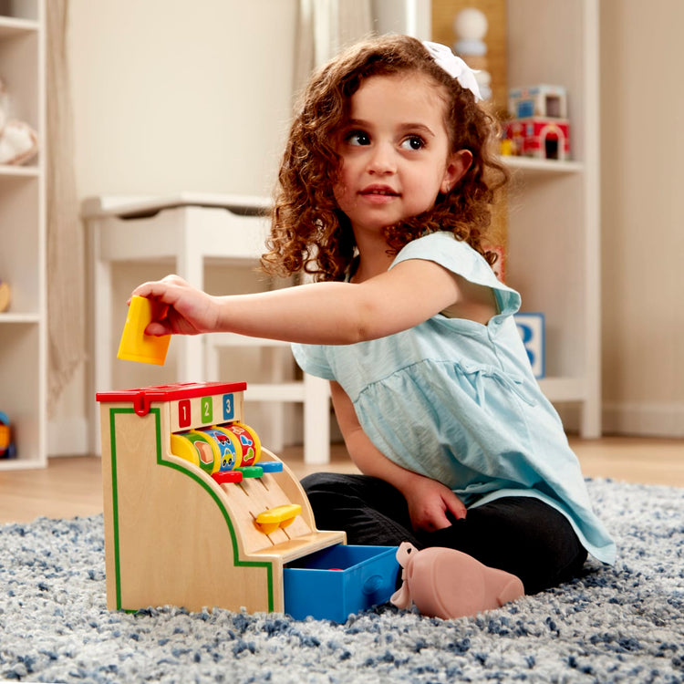 A kid playing with the Melissa & Doug Spin and Swipe Wooden Toy Cash Register With 3 Play Coins, Pretend Credit Card