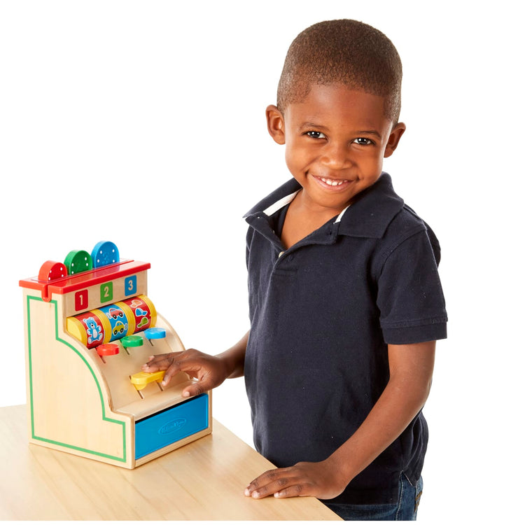 A child on white background with the Melissa & Doug Spin and Swipe Wooden Toy Cash Register With 3 Play Coins, Pretend Credit Card