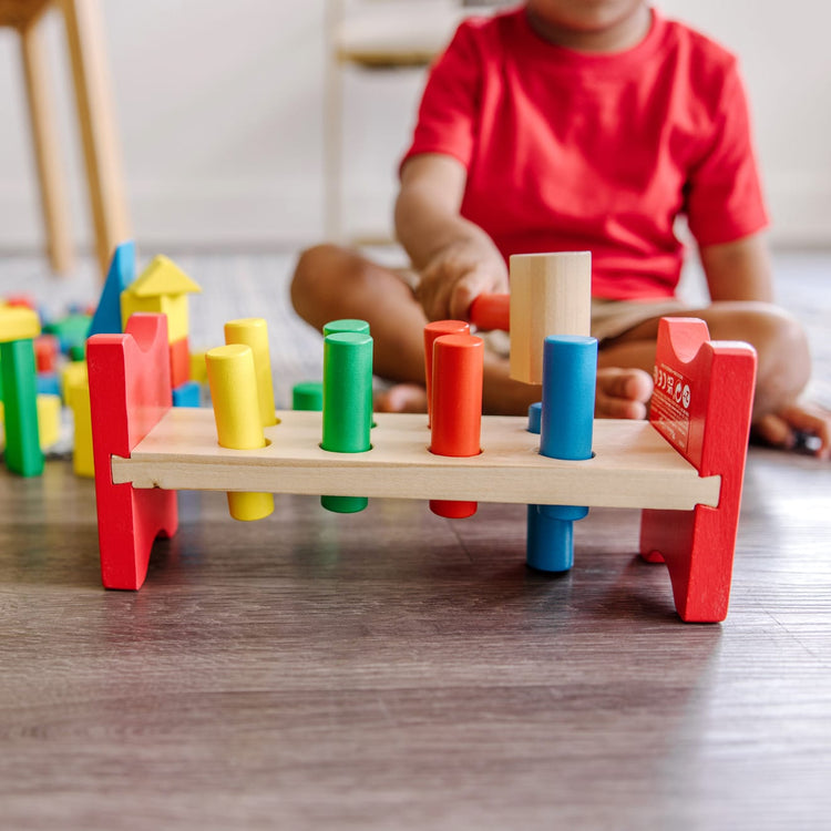 A kid playing with the Melissa & Doug Stack, Sort & Pound Wooden Toy Collection (Building Blocks, Shape Sorter, Pounding Bench)
