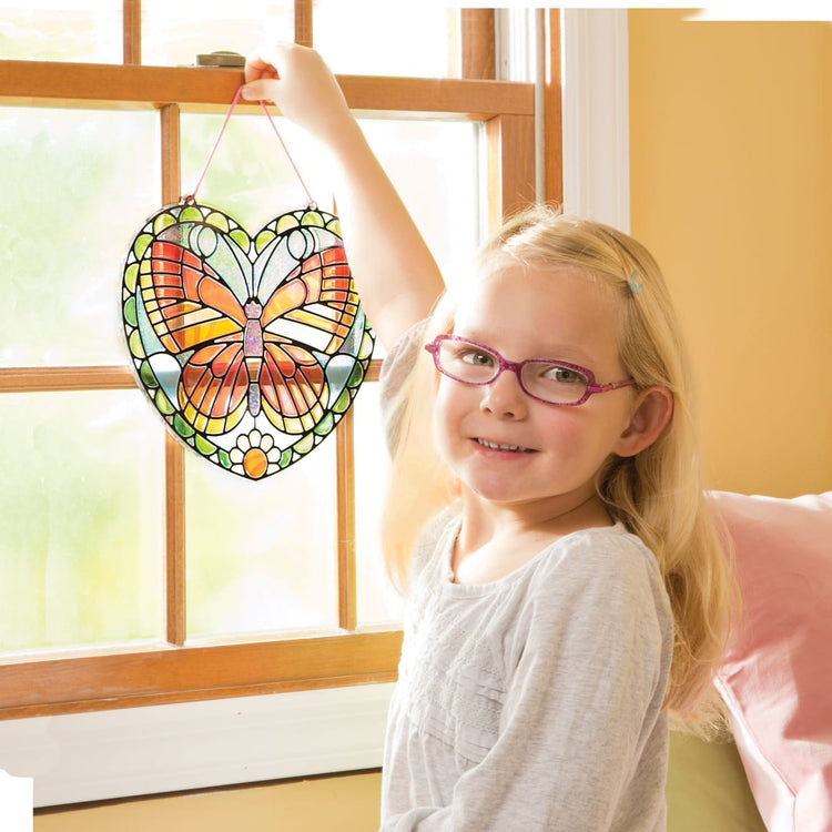 A kid playing with the Melissa & Doug Stained Glass Made Easy Activity Kit: Butterfly - 140+ Stickers