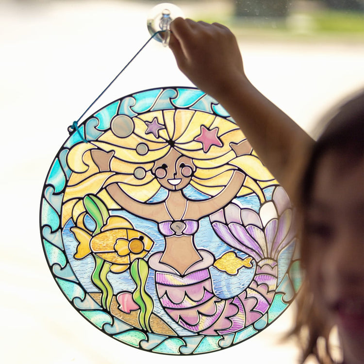 A kid playing with the Melissa & Doug Stained Glass Made Easy Activity Kit: Mermaids - 140+ Stickers